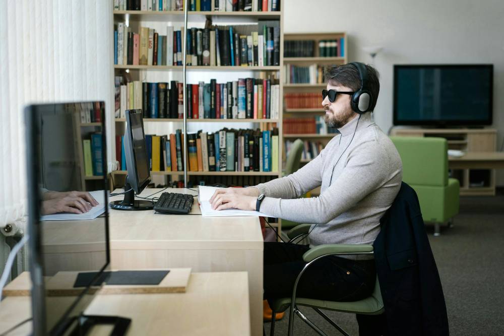 A person working at a computer with sunglasses and a headset on
