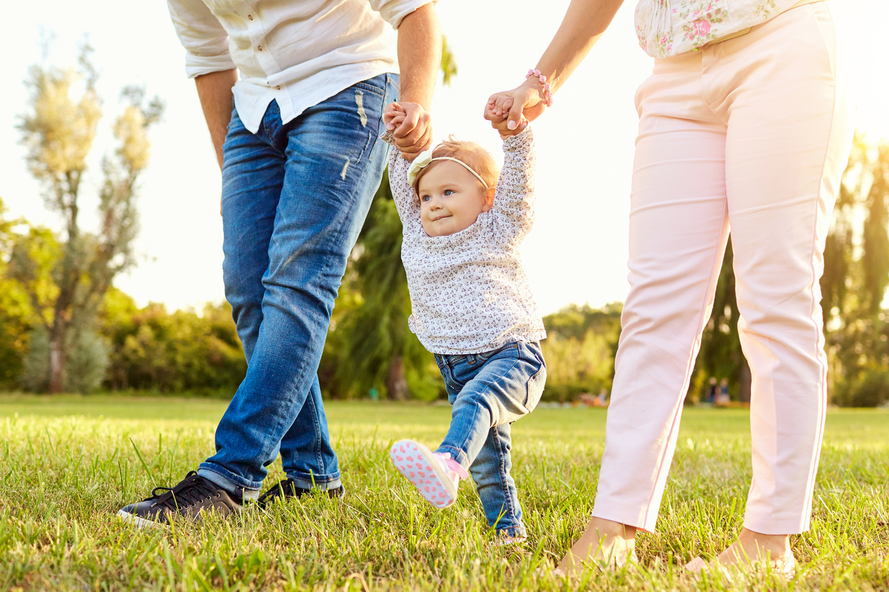 Parents helping toddler walk outside