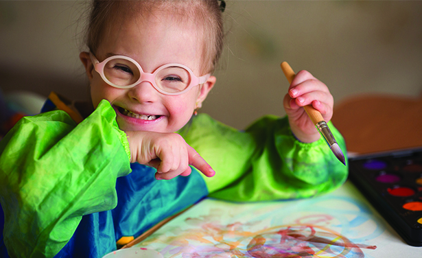 Girl with glasses smilining and pointing to the painting she is making