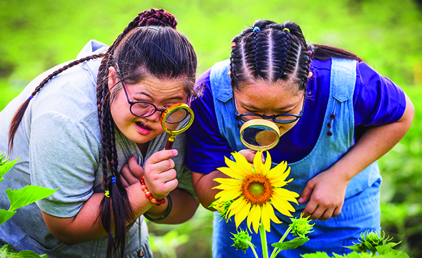 two girls observe a flower with magnifying glasses