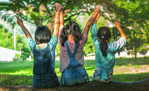 three children sit on a tree and raise their hands in joy