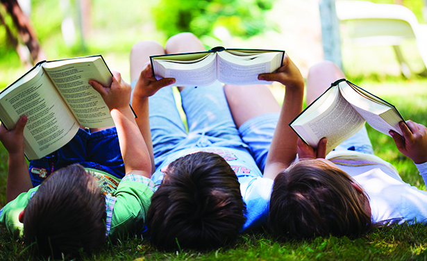 three children lay on the grass while reading books