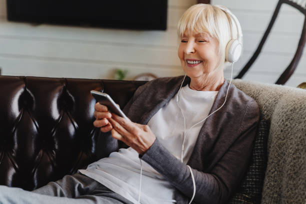 Older woman on couch listening to tablet using headset. 