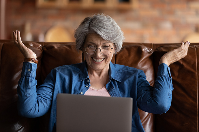 An older woman sitting on a couch talking with someone via her laptop.