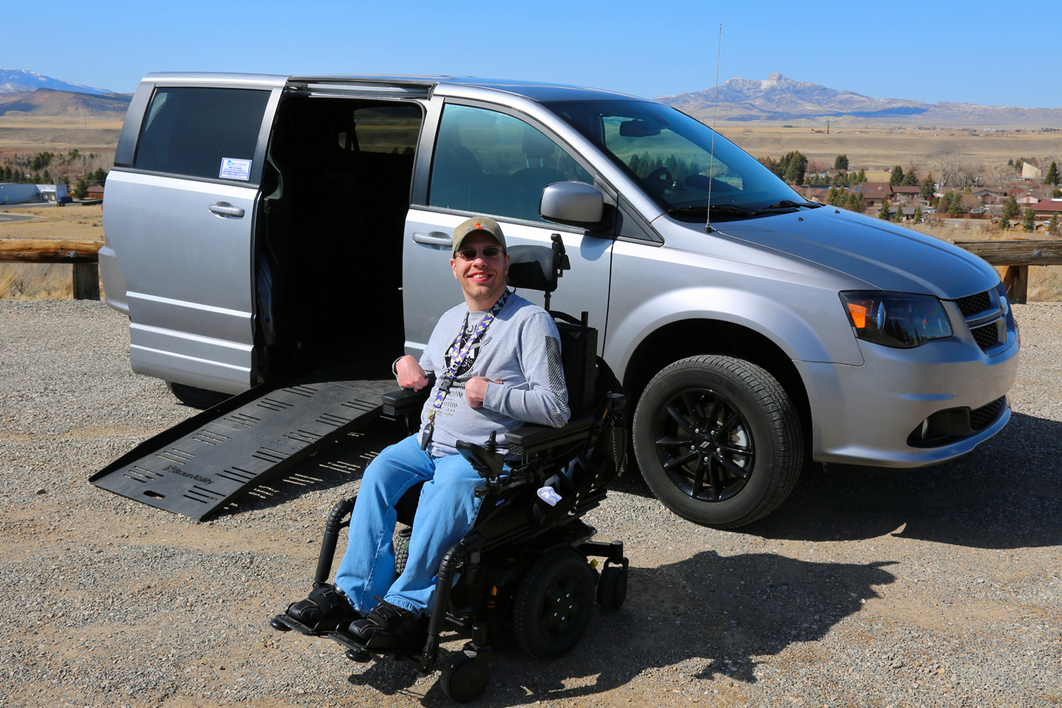 accessible van with ramp and man using a powerchair next to ramp with mountains in the background