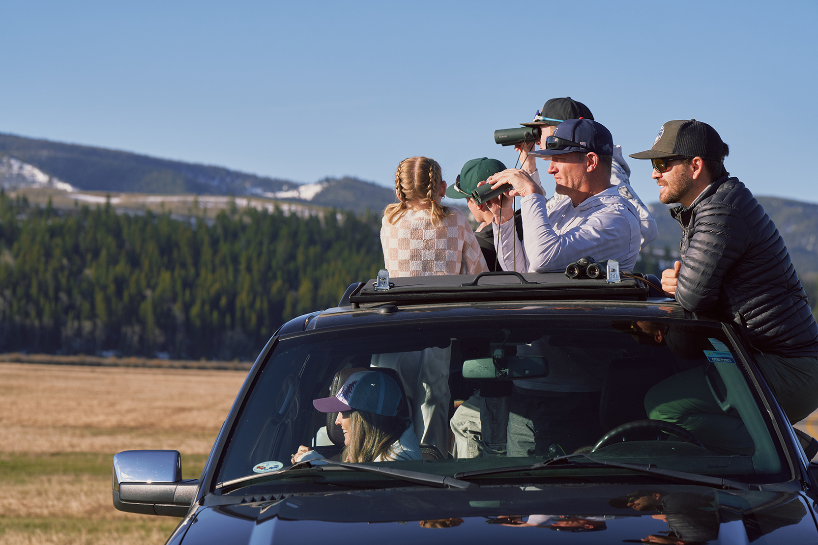 Tourists looking through binoculars on top of car