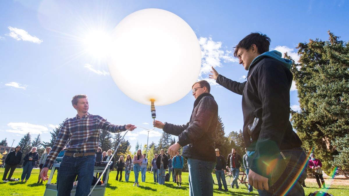 Three students let go of a weather balloon on Prexy's Pasture as a crowd looks on.