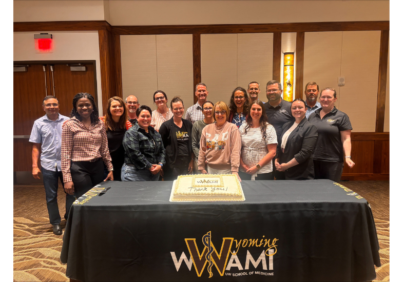 The staff and faculty with WWAMI standing as a group next to a cake on a table.