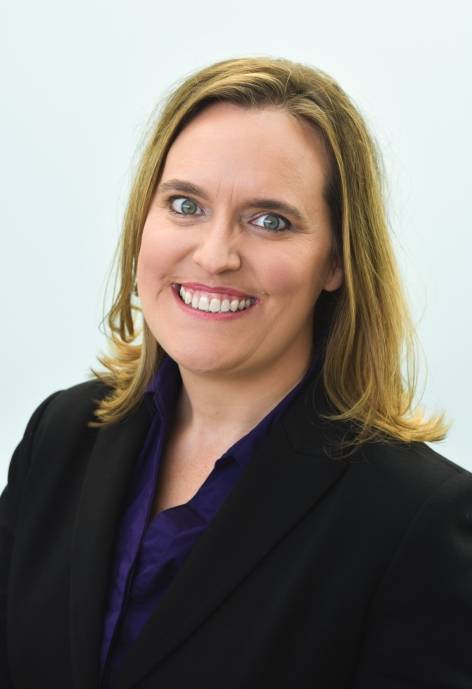 April French, wearing a black suit jacket and a dark purple blouse.