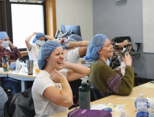 Students sitting at desks trying on medical hair nets and laughing.