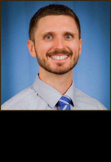 Dr. Samuel Hart, wearing a light grey button-up shirt and a blue tie.