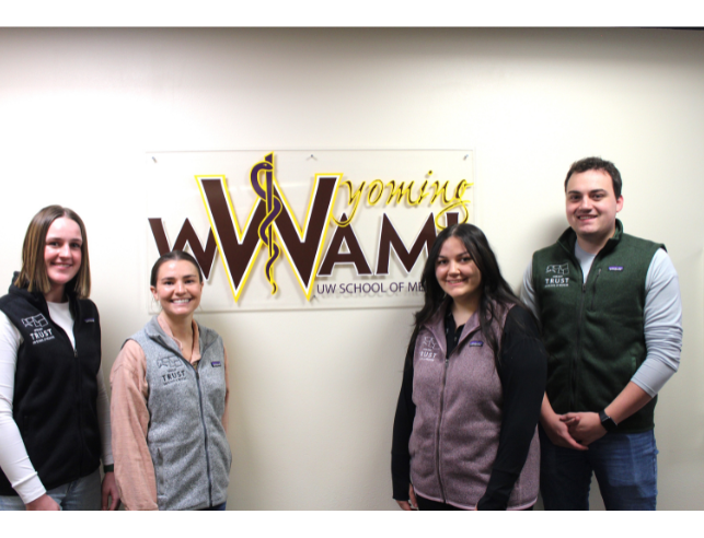 Four students stand next to a glass sign that says, "Wyoming WWAMI - School of Medicine."