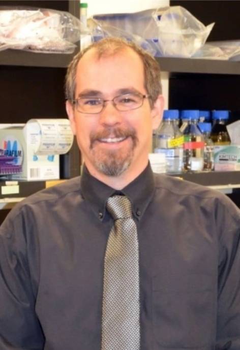 Brian Cherrington, wearing a dark grey button-up shirt and a silver tie.