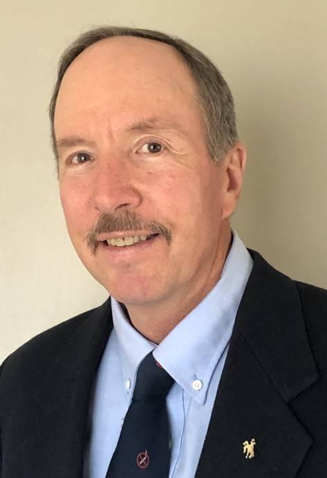 Dan Radosevich, wearing a black suit jacket, a light blue button-up shirt, and a dark blue tie.