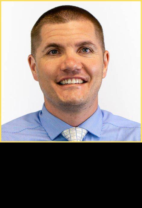 Dr Derek Ewell, wearing a blue button-up shirt and a white tie.