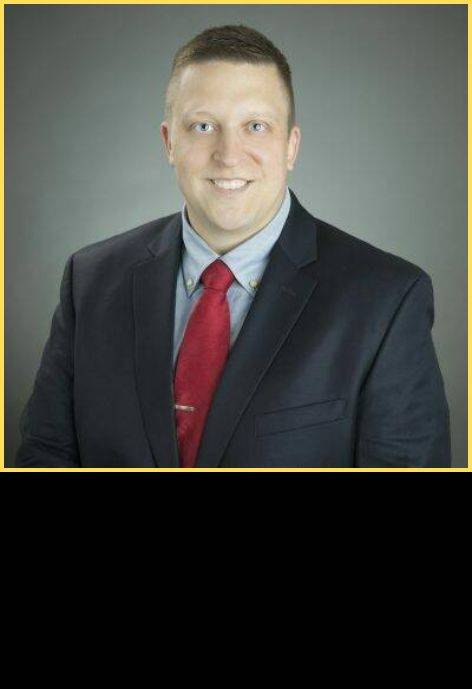 Dr. John Horberg; wearing a black suit jacket, light blue button-up shirt, and a red tie.