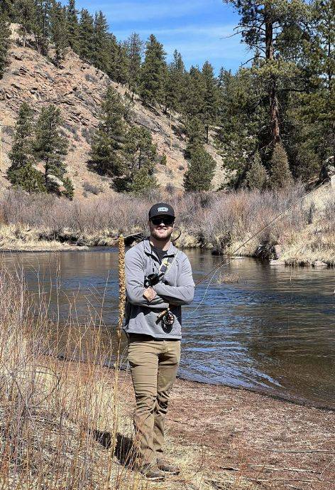 Trent Bronnenberg standing on the bank of a river, fishing.