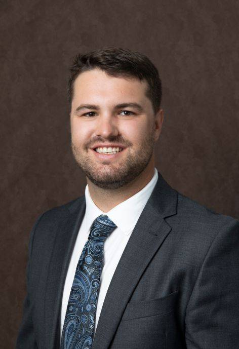 Trent Bronnenberg, wearing a dark blue suit jacket, white button-up, and a blue patterned tie.