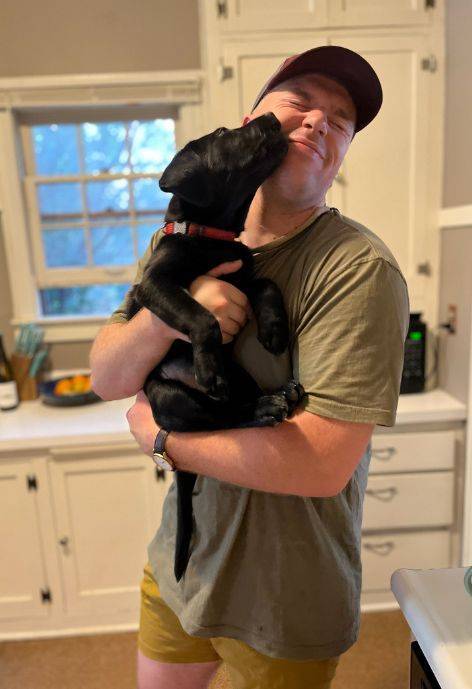 Aaron Erickson, holding a puppy while it licks his face.