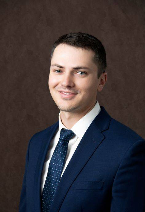 Brayden Feusner, wearing a dark blue suit jacket, white button-up, and dark blue tie.