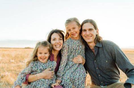 Cale Hinkle with his wife and two daughters, they are standing in a field and smiling at the camera.
