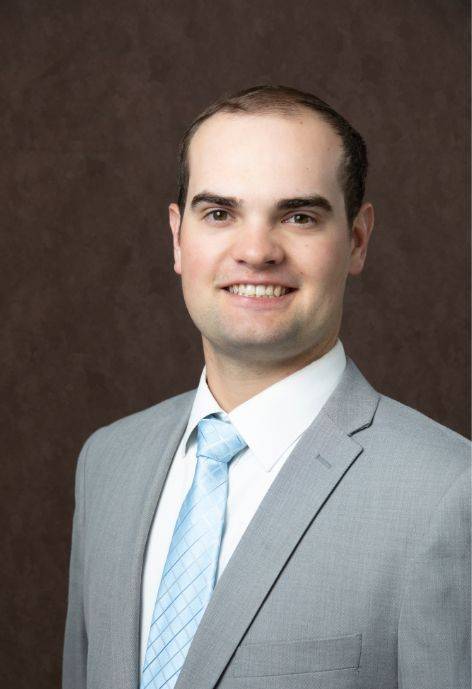 Caleb Hoopes, wearing a light grey suit jacket, white button-up, and a light blue tie.
