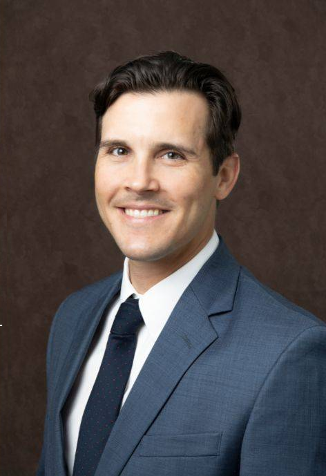 Casey Pikla wearing a blue suit jacket, white button-up, and dark blue tie.