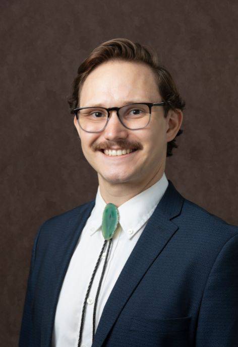 Galen Tribble wearing a dark blue suit jacket, white button-up, and a green bolo tie.