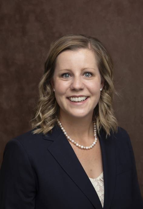 Brandi Carreau wearing a dark blue jacket, white blouse, and pearl necklace.
