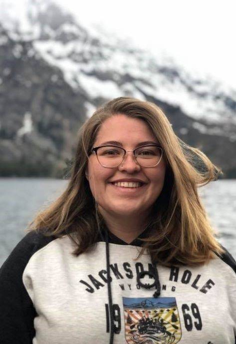 Annaliese standing outside with a snow covered mountain and lake behind her.