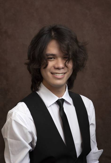 Dean He wearing a black suit vest, white button-up, and black tie.