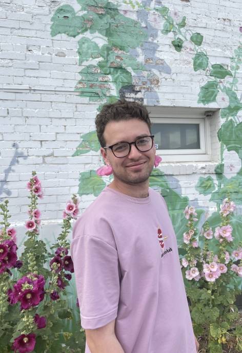 Rafael standing next to a garden with hollyhocks.