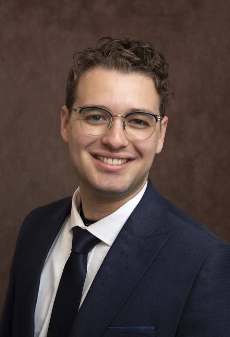 Rafael Homer wearing a dark blue jacket, white button-up, and dark blue tie.