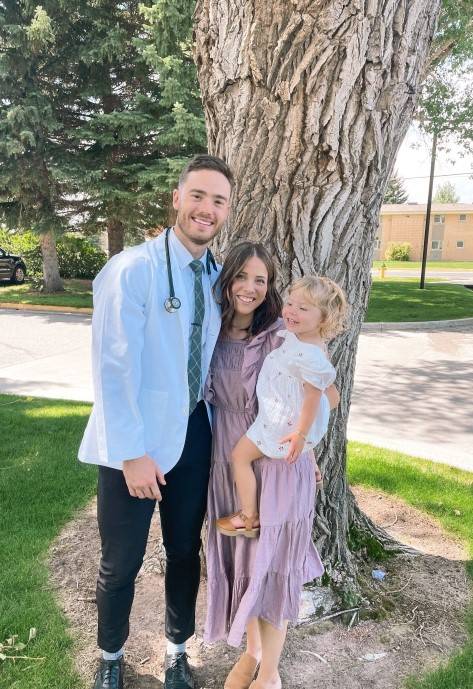 Kaden with his wife and daughter, standing next to a large tree trunk.