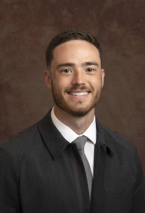 Kaden Moore wearing a dark grey suit jacket, white button-up, and light grey tie.