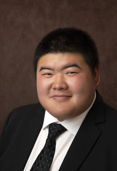 Sai Kit Ng wearing a black suit jacket, white button-up, and black tie.