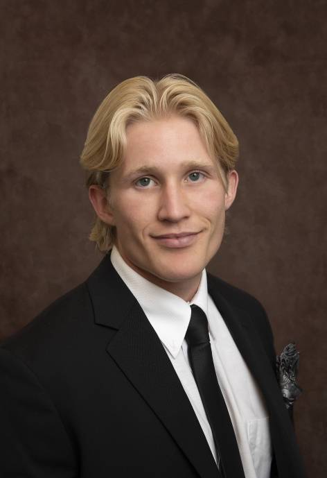 Aaron Nichols wearing a black suit jacket, white button-up, and black tie.