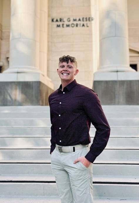 Matthew standing on a white stone staircase and smiling at the camera.