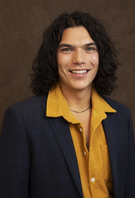 Kyler Arriola wearing a dark blue suit jacket and a yellow corduroy button-up shirt.