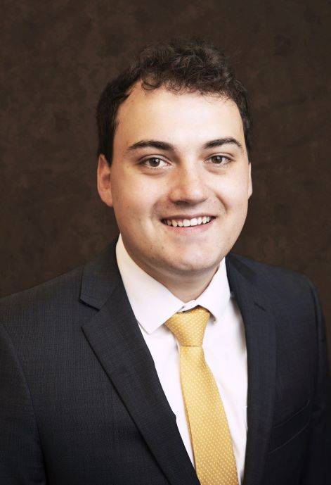Caden Crooks wearing a dark blue suit jacket, white button-up, and yellow tie.