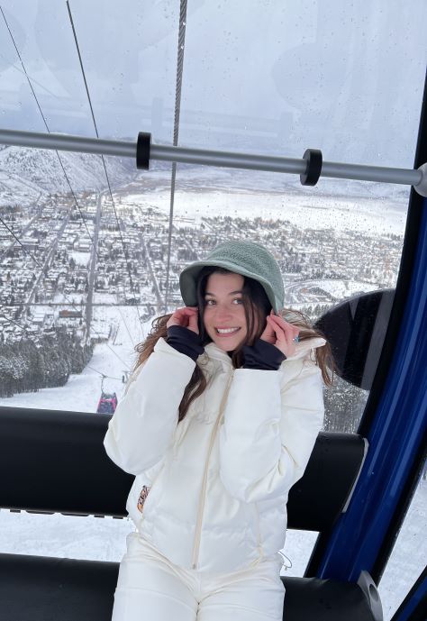 Cassidy wearing a white snow suit and sitting in a ski lift.