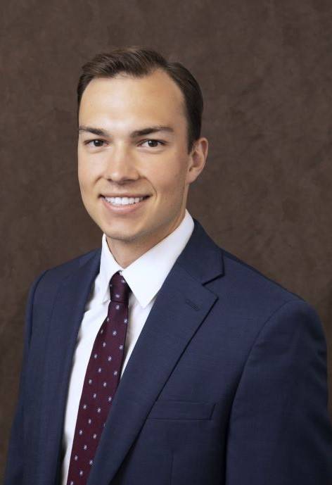 Tim Radosevich wearing a blue suit jacket, white button-up, and a dark purple tie.