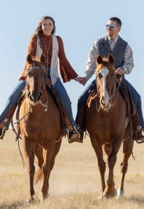 Sarah on a horse holding hands with a man also on a horse.