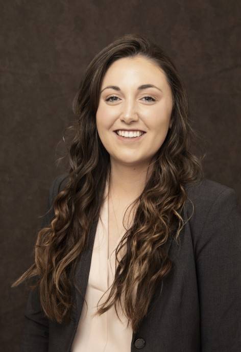 Sarah Retherford wearing a dark grey jacket and a light pink blouse.