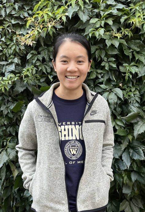 Lulu standing in-front of a wall of plants and smiling at the camera.