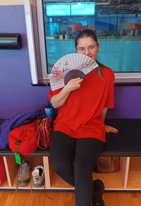 Hannah posing with a fan sitting on a bench at a gym.