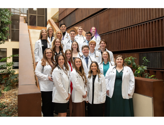 A group of 20 students wearing doctor coats and standing together on a staircase.