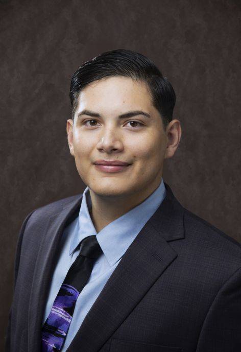Carlos Garcia wearing a black suit jacket, blue button-up, and purple patterned tie.