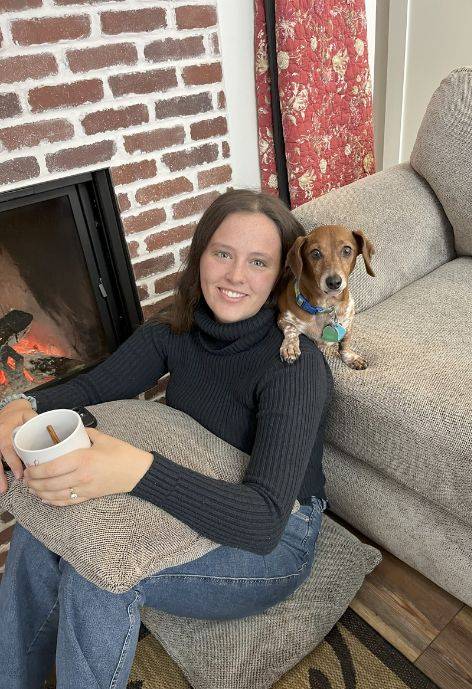 Elizabeth sitting on the ground while a small dog stands behind her on a couch.