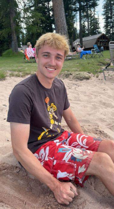 Logan sitting on a sandy beach with a park in the background.